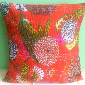 May include: Red cotton pillow cover with a floral pattern in shades of brown, green, white, and pink. The pillow cover is quilted with white thread.