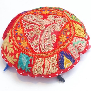 Puede incluir: Cojín de suelo redondo rojo con intrincados bordados y diseño de patchwork. El cojín presenta detalles dorados, azules y verdes, con un patrón central en forma de cachemira. Borlas decorativas están unidas alrededor del borde.