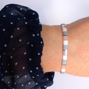 Könnte beinhalten: Ein Armband aus kleinen, quadratischen Fliesen in Grautönen, Weiß und Rosa. Die Fliesen sind in einem sich wiederholenden Muster angeordnet.