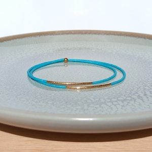 Könnte beinhalten: Ein türkisfarbenes und goldenes Armband. Das Armband besteht aus zwei Reihen türkisfarbener Perlen mit einer einzelnen Reihe goldener Perlen dazwischen.