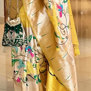 May include: A yellow and gold silk saree with a floral print and a green embroidered pouch bag.