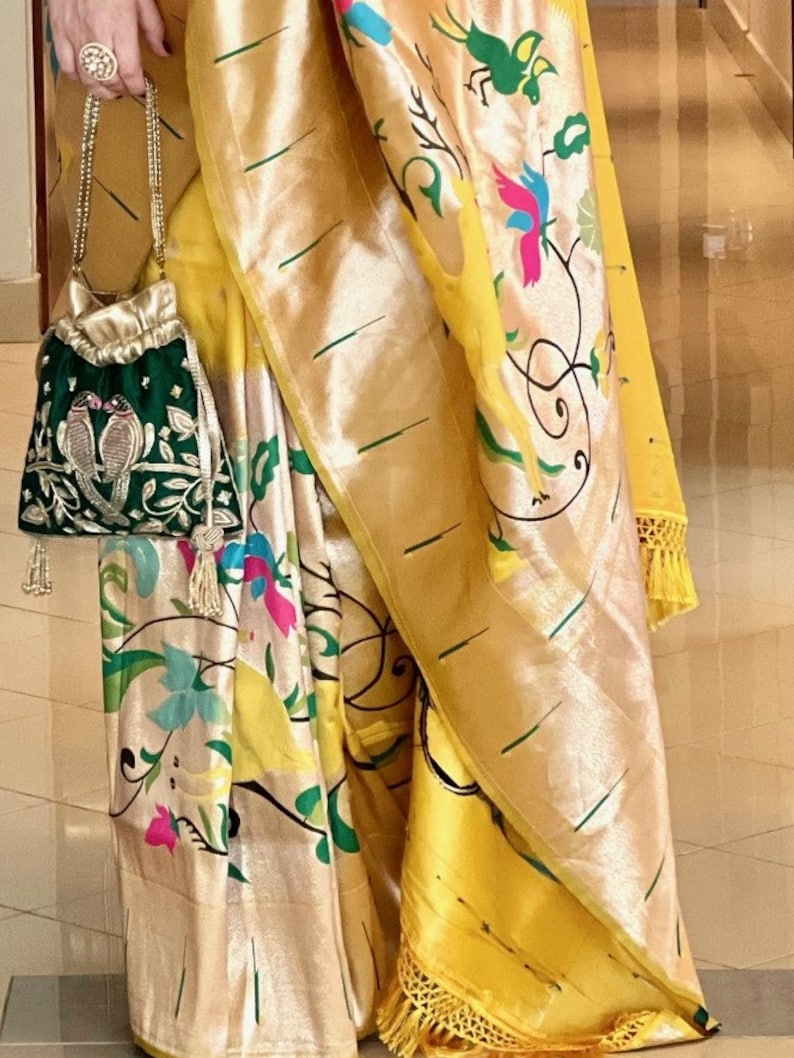 May include: A yellow and gold silk saree with a floral print and a green embroidered pouch bag.