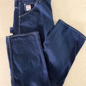 May include: Dark blue denim work pants with white stitching and a small pocket on the front. The pants have a straight leg design and a label that reads "Pointer".