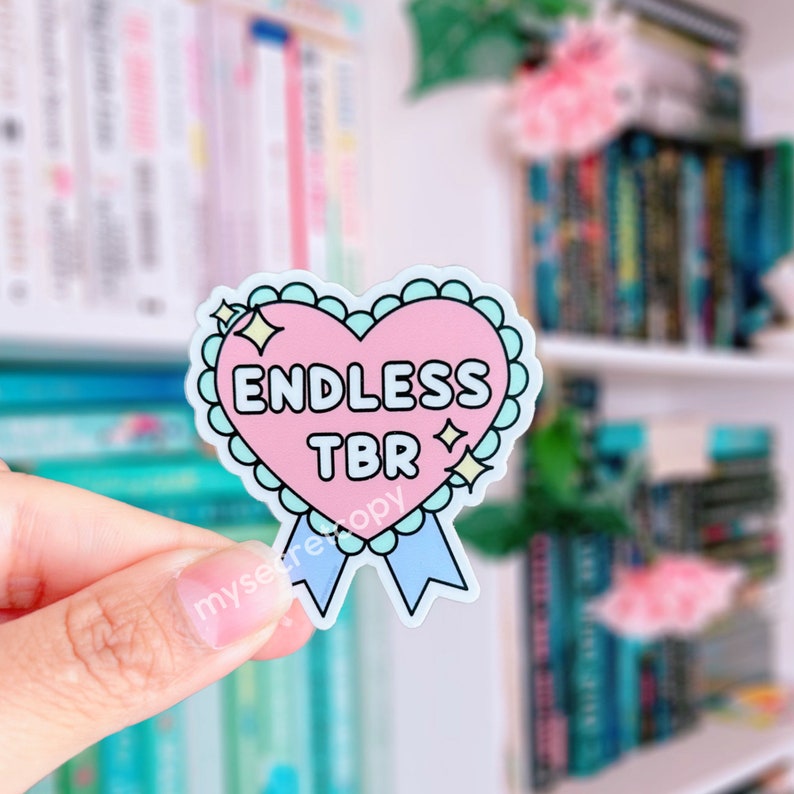 May include: A pink heart-shaped sticker with a blue ribbon and the text "ENDLESS TBR" in black lettering. The sticker is on a white background.
