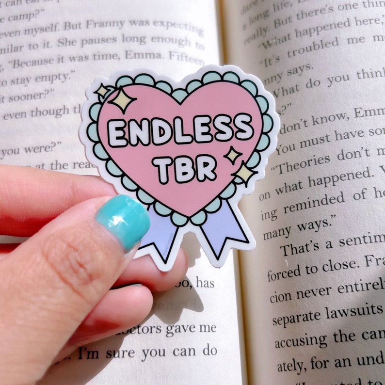 May include: A pink heart-shaped sticker with a white outline and a blue ribbon. The sticker says "ENDLESS TBR" in white text.