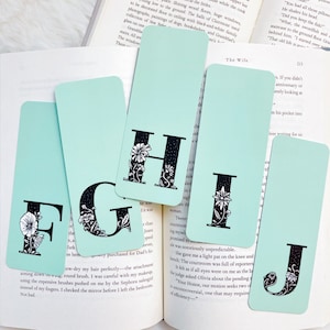 May include: Four bookmarks with a light blue background and black floral designs. Each bookmark features a different letter of the alphabet: F, G, H, and J. The letters are in a black, bold font with a white outline.
