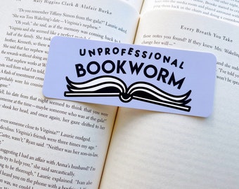 May include: A light blue bookmark with the text "Unprofessional Bookworm" in black lettering. The bookmark features a stylized image of an open book with curled pages.