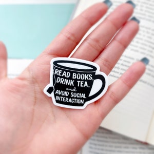 May include: A white sticker with a black outline of a teacup. The teacup has text that reads "READ BOOKS, DRINK TEA, and AVOID SOCIAL INTERACTION."