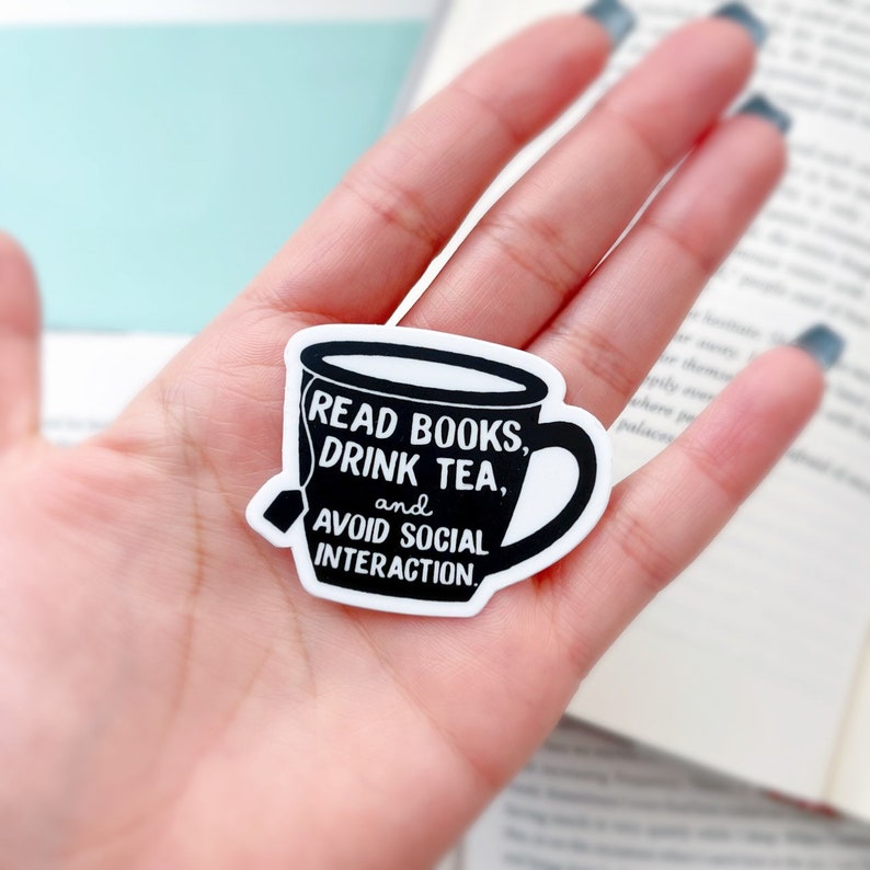 May include: A white sticker with a black outline of a teacup. The teacup has text that reads "READ BOOKS, DRINK TEA, and AVOID SOCIAL INTERACTION."