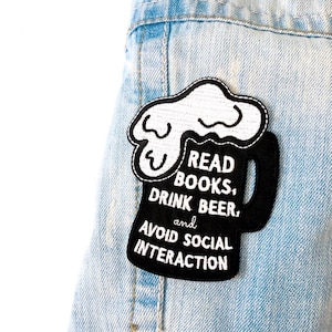 Puede incluir: Parche de hierro bordado en blanco y negro con un diseño de jarra de cerveza. El texto dice "Leer libros, beber cerveza y evitar la interacción social."