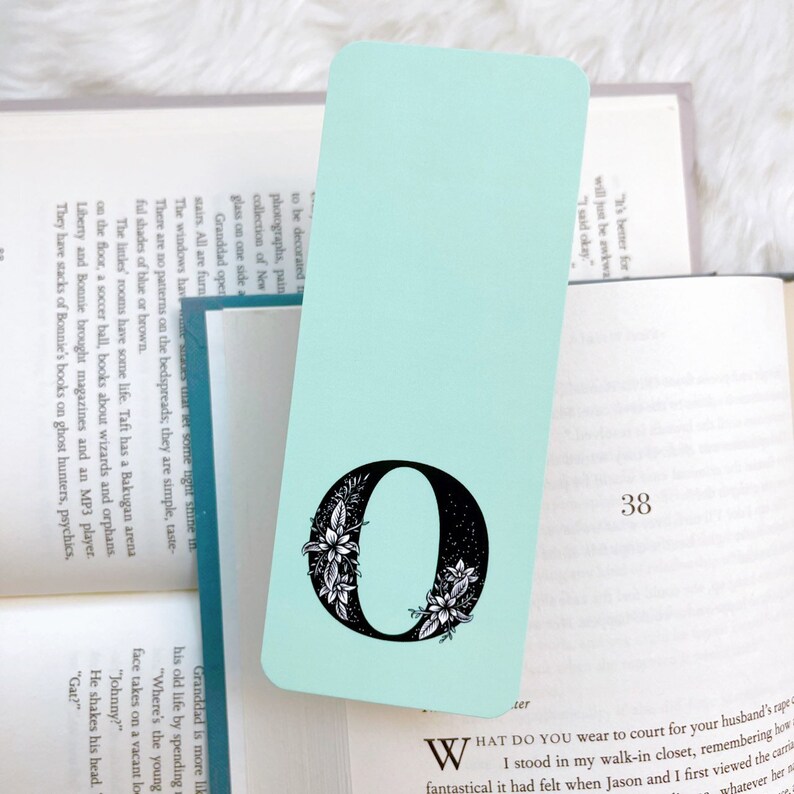 May include: A light blue bookmark with a black floral design around the letter "O".