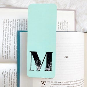 May include: A light blue bookmark with a black letter M and floral design. The bookmark has the text "Three Days Later" at the bottom.