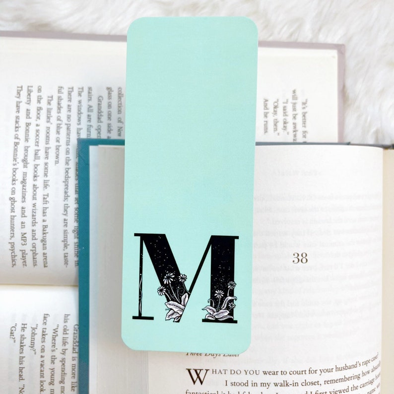 May include: A light blue bookmark with a black letter M and floral design. The bookmark has the text "Three Days Later" at the bottom.