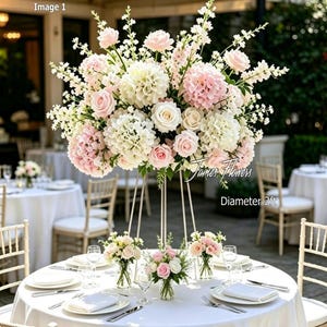 May include: A large floral centrepiece featuring white and light pink roses, hydrangeas, and tall white snapdragons arranged on a tall, thin metal stand. The arrangement has a diameter of 2ft. Three smaller matching floral vases sit on the table.