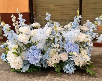 Peut inclure: Composition florale avec des roses blanches, des hortensias bleus et d'autres fleurs bleues et blanches. L'arrangement est dense et vibrant, avec des feuilles vertes à la base. Le texte "James Flower" est visible.