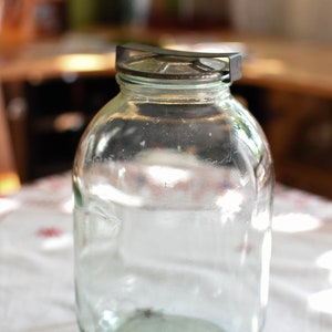 Puede incluir: Un tarro de vidrio transparente con una tapa de metal. El tarro está vacío y tiene una superficie ligeramente texturizada.