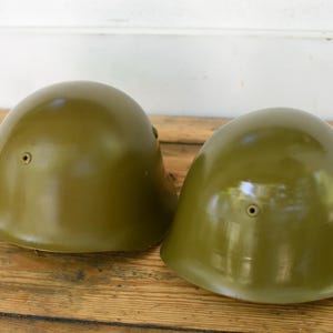 May include: Two olive green military helmets with a leather strap on one helmet.