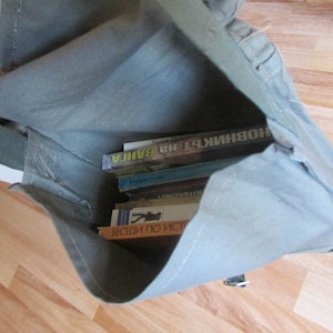 May include: A gray canvas bag with a zipper closure and a strap. The bag is filled with several books, including one with the title "BAHIA" in Russian.