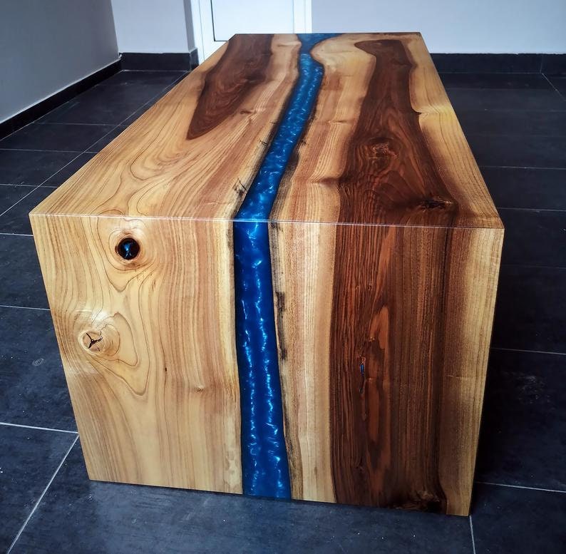 Puede incluir: Una mesa de centro de madera con un r&iacute;o de resina azul que atraviesa el centro. La mesa est&aacute; hecha de madera clara y oscura.
