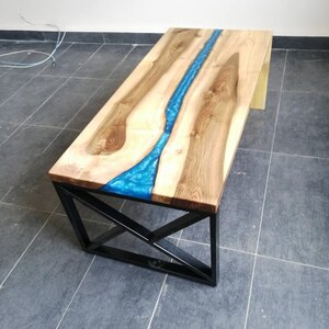 Puede incluir: Una mesa de centro de madera con un r&iacute;o de resina azul que recorre el centro. La mesa tiene un marco de metal negro con un dise&ntilde;o geom&eacute;trico.