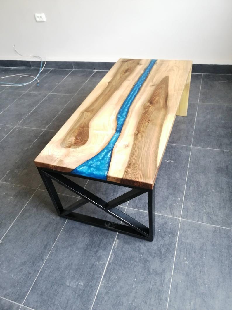 Puede incluir: Una mesa de centro de madera con un r&iacute;o de resina azul que recorre el centro. La mesa tiene un marco de metal negro con un dise&ntilde;o geom&eacute;trico.