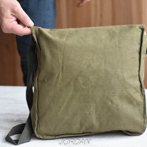May include: A green canvas messenger bag with a black adjustable strap. The bag has a flap closure and a zippered pocket on the front.