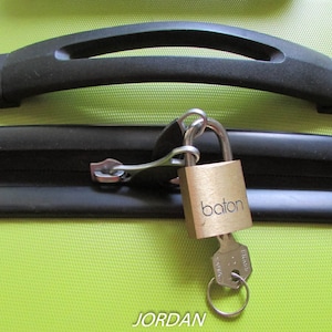 May include: A gold padlock with the word "baton" printed on it is attached to a black zipper on a green suitcase.