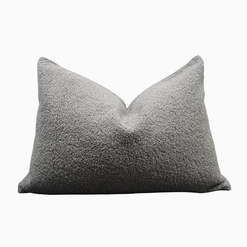 May include: A gray decorative pillow with a textured, plush surface. The pillow has a rectangular shape with a pointed top and bottom. The pillow is a solid, neutral color, suitable for various home decor styles.