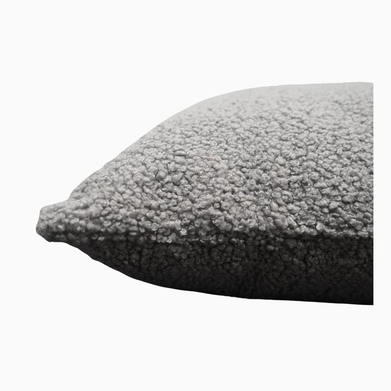 May include: A close-up of a gray, textured pillow. The pillow has a soft, plush appearance with a dense, looped fabric. The color is a neutral gray, suitable for various home decor styles.