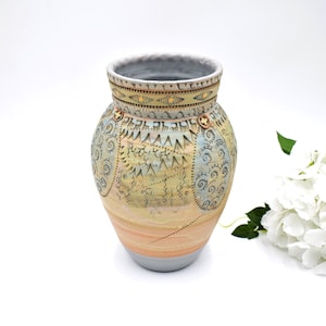 May include: A ceramic vase with a light brown, yellow and blue geometric pattern. The vase has a wide mouth and a rounded body.