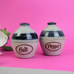 May include: A set of two ceramic salt and pepper shakers with blue and white stripes. The shakers are labelled "Salt" and "Pepper".