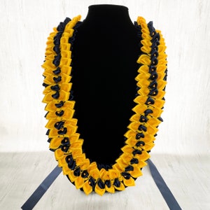 May include: A yellow and navy blue lei made of satin ribbon. The lei is arranged in a traditional style with alternating colors and is displayed on a black mannequin.