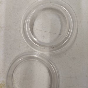 May include: Two clear plastic rings, one larger than the other, on a white surface.