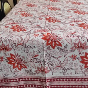 May include: White tablecloth with a red and pink floral pattern. The tablecloth has a red border with a white geometric design.