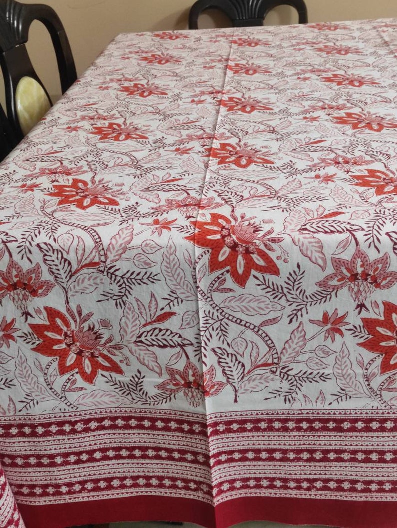 May include: White tablecloth with a red and pink floral pattern. The tablecloth has a red border with a white geometric design.