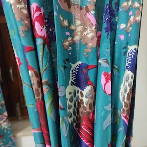 Puede incluir: Tela color turquesa con un vibrante estampado floral y de p&aacute;jaros. El dise&ntilde;o presenta p&aacute;jaros coloridos, flores rosas y rojas y hojas verdes. La tela est&aacute; drapeada, mostrando los intrincados detalles del estampado.