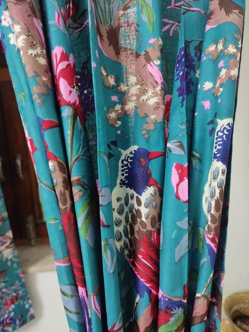 Puede incluir: Tela color turquesa con un vibrante estampado floral y de p&aacute;jaros. El dise&ntilde;o presenta p&aacute;jaros coloridos, flores rosas y rojas y hojas verdes. La tela est&aacute; drapeada, mostrando los intrincados detalles del estampado.