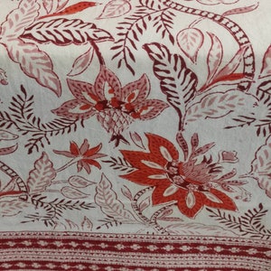 May include: White fabric with a red and pink floral print. The fabric has a red border with a white and red pattern.
