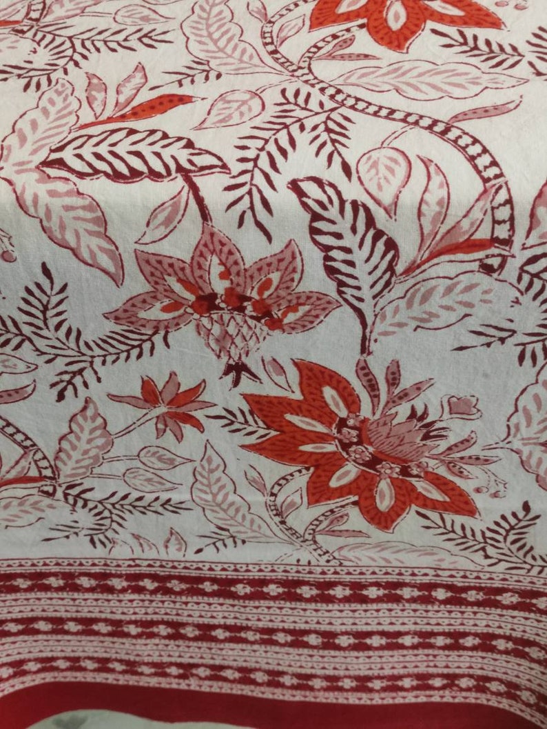 May include: White fabric with a red and pink floral print. The fabric has a red border with a white and red pattern.