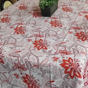 May include: White tablecloth with a red and brown floral pattern. The tablecloth has a red border with a white pattern.