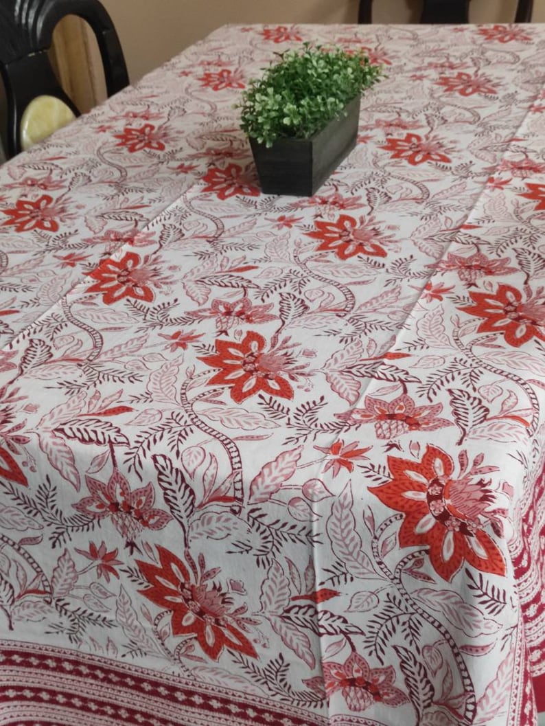 May include: White tablecloth with a red and brown floral pattern. The tablecloth has a red border with a white pattern.