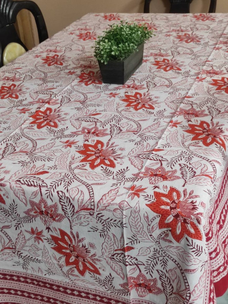 May include: White tablecloth with a red floral pattern. The tablecloth has a border of red and white.
