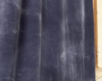 Puede incluir: Primer plano de una cortina de terciopelo azul marino con pliegues verticales. La tela tiene un aspecto suave y texturizado con sutiles variaciones de color, creando una sensación de profundidad. La cortina está parcialmente iluminada, revelando su rico color y lujosa textura.