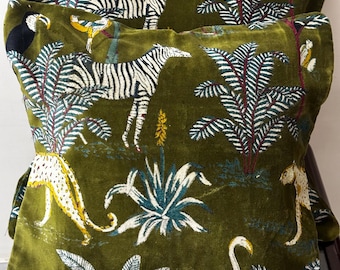 May include: A square velvet throw cushion in olive green featuring an embroidered jungle scene. The design includes a zebra, a leopard, a toucan, and a flamingo surrounded by palm trees and tropical foliage in shades of white, black, and yellow.