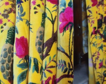 May include: Yellow velvet curtains with a floral pattern in shades of pink, green, and brown. The pattern features stylised flowers, leaves, and branches.