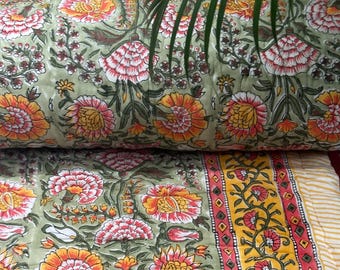 May include: A floral patterned quilt in shades of green, yellow, orange, and pink. The quilt features a repeating pattern of large flowers and foliage. The border is yellow with a red floral design. The quilt is folded over.