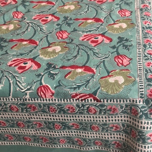 May include: A green tablecloth with a floral pattern featuring red and green flowers. The tablecloth has a border with a repeating pattern of small pink flowers.