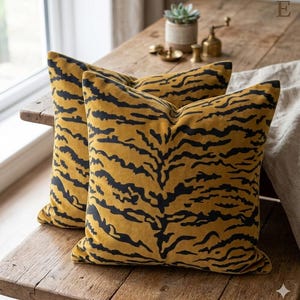 May include: Two square throw pillows featuring a mustard yellow velvet fabric with a black tiger stripe pattern. The pillows are plush and have a soft texture, displaying a consistent animal-inspired print across the front surfaces.