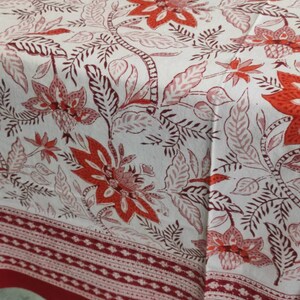 May include: White tablecloth with a red and pink floral pattern. The tablecloth has a red border with a white geometric design.