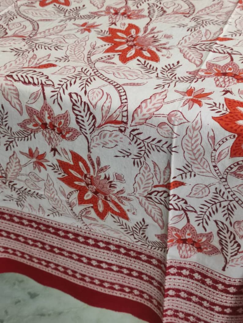 May include: White tablecloth with a red and pink floral pattern. The tablecloth has a red border with a white geometric design.